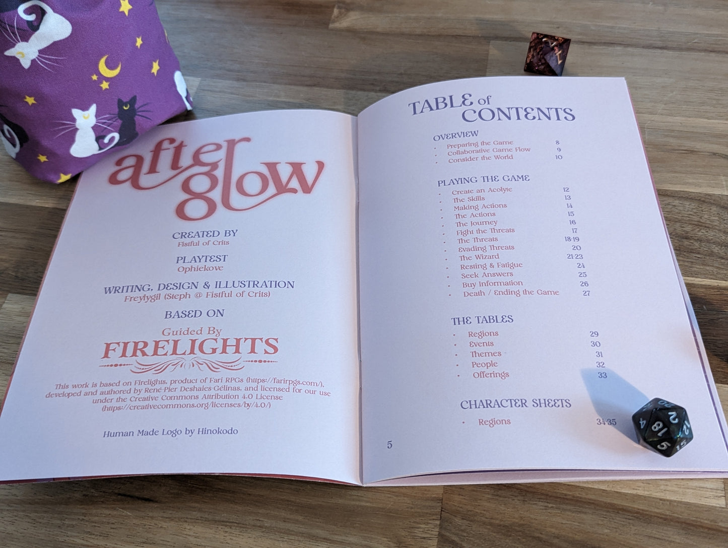 Afterglow open on a table, weighed down by a dice bag, a d20 and a d8 dice